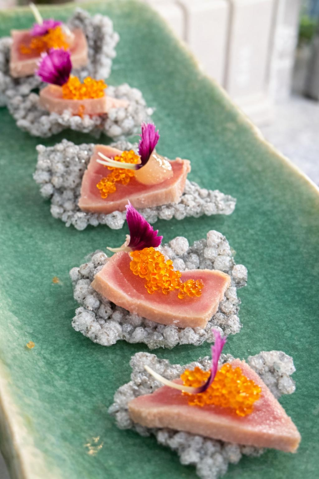 Seared tuna on crisp tapioca crackers with roe and petals on a green plate