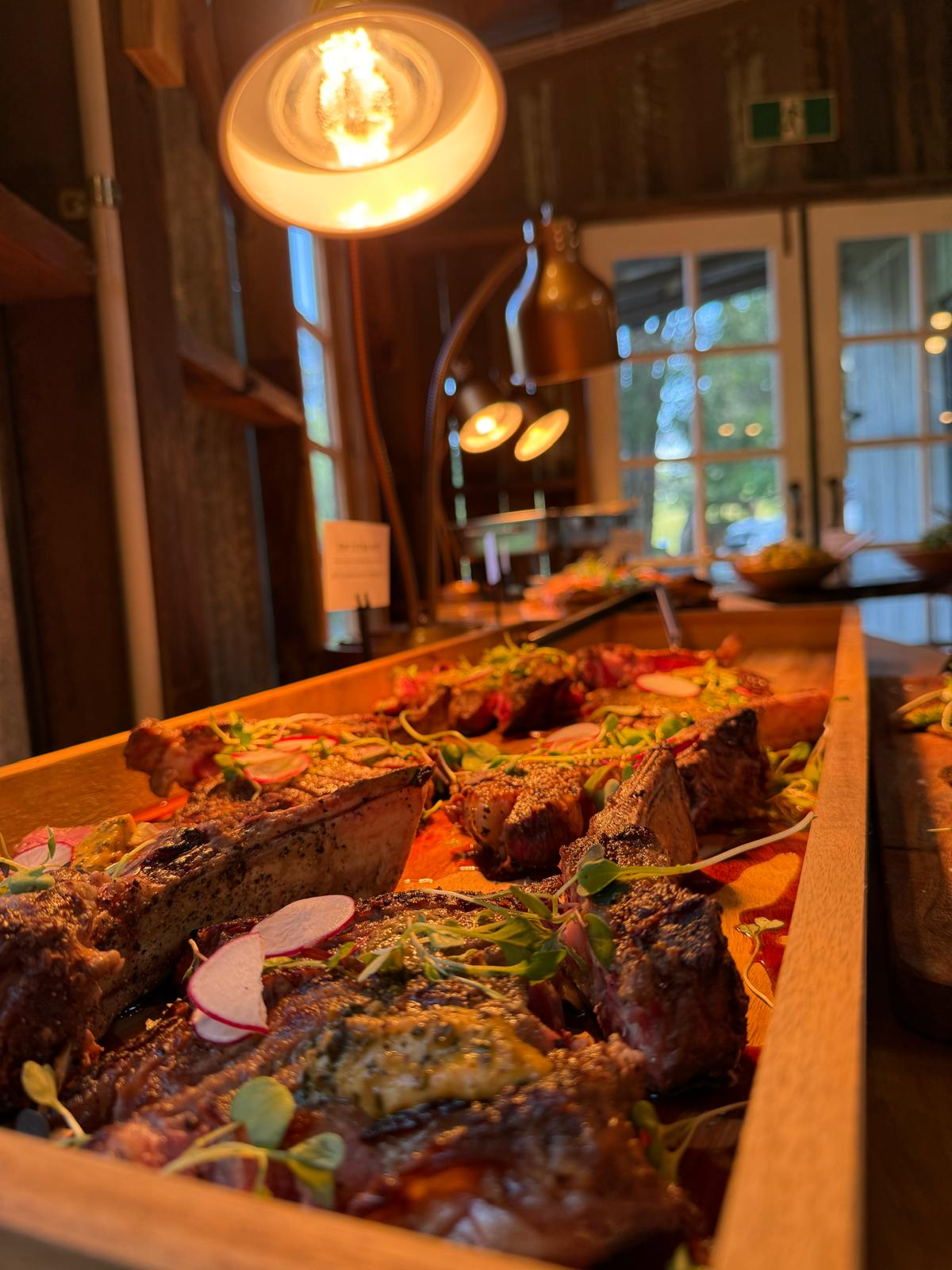 Shared banquet board of pork belly and grilled meats under warm heat lamps