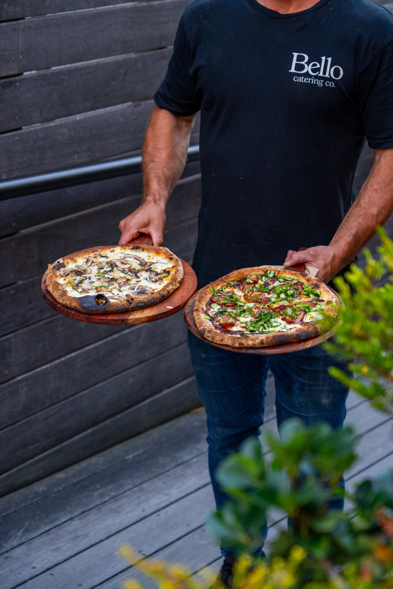 Bello chef carrying a wild mushroom pizza and a shredded duck pizza on timber boards