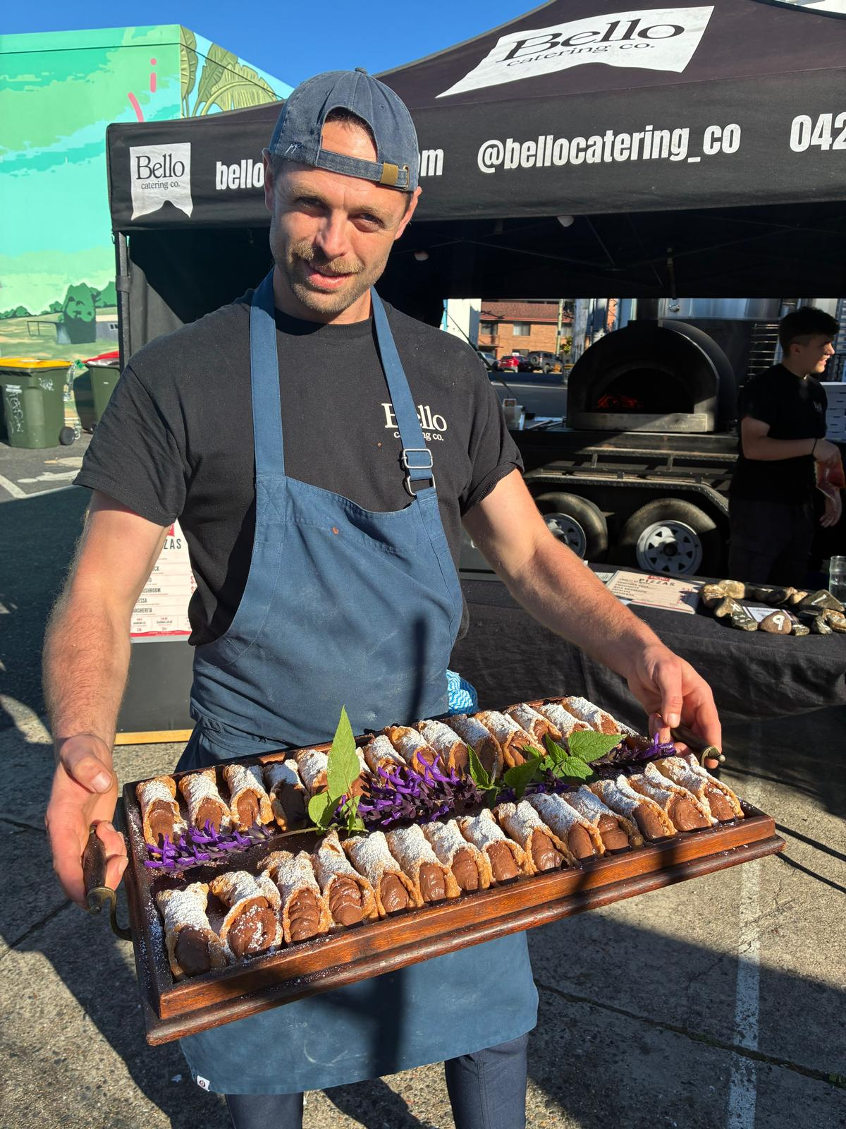Bello team member holding a timber board of chocolate-filled cannoli dusted with icing sugar