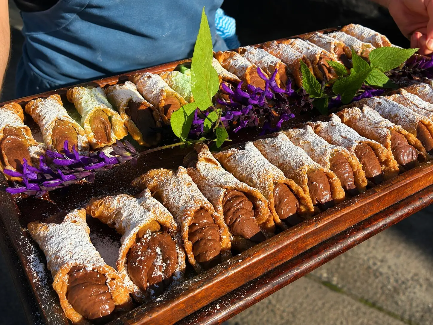 Trays of chocolate-filled cannoli dusted with icing sugar at a Bello event