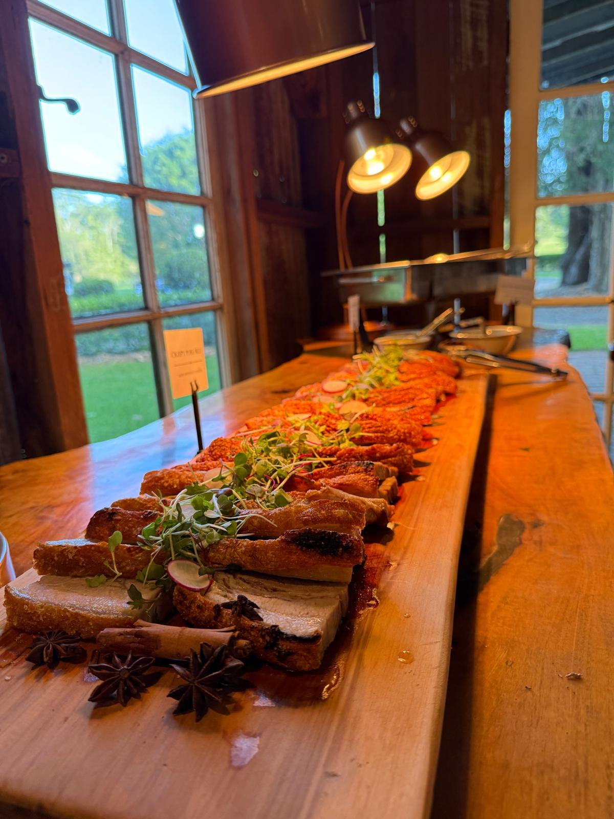 Shared banquet board of crispy pork belly with greens on a timber table