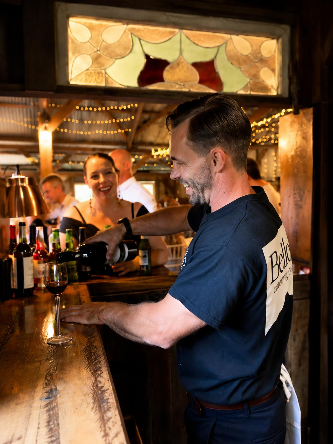 Bello bartender pouring red wine at the mobile bar under string lights