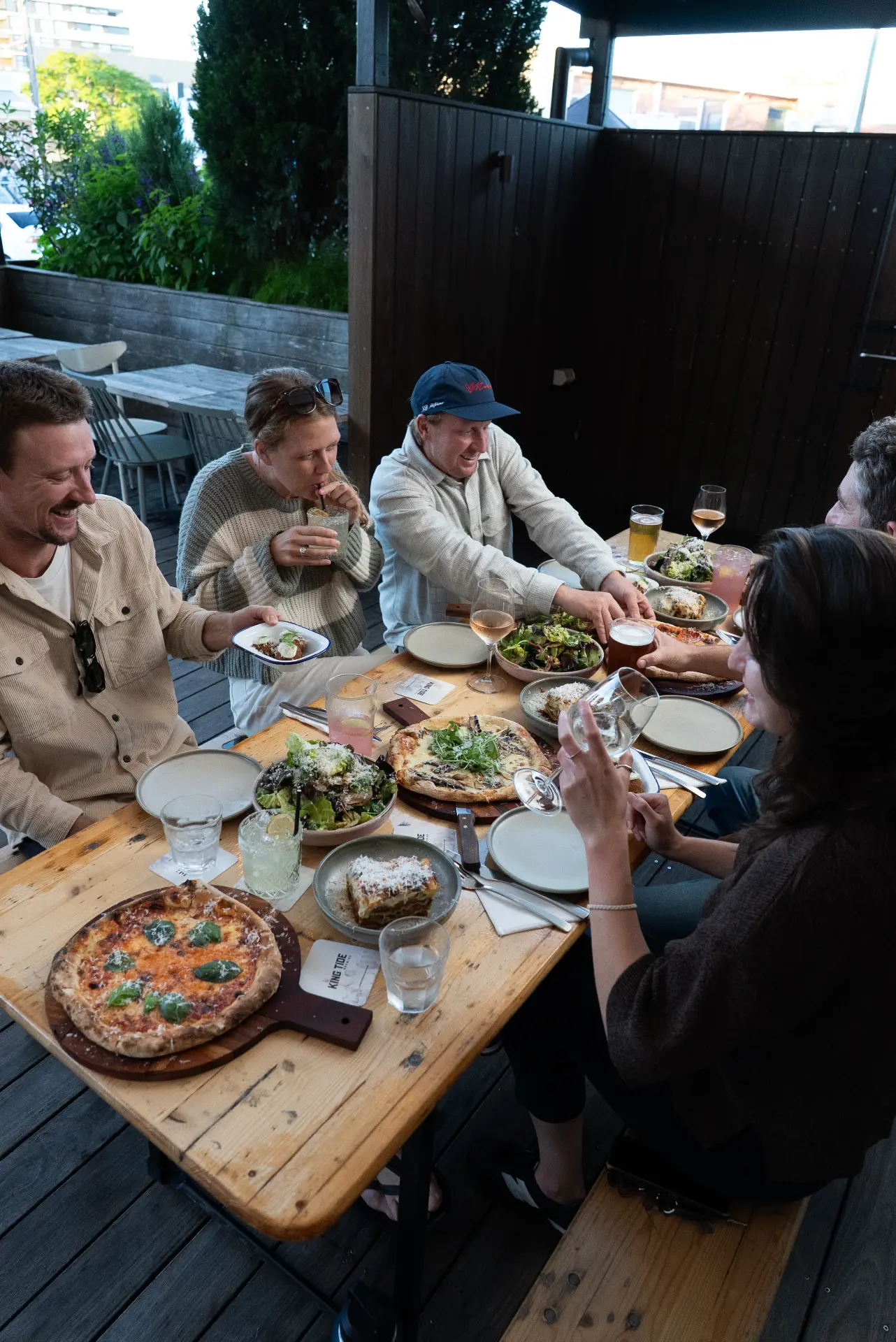 Guests sharing pizza and drinks around a long timber table
