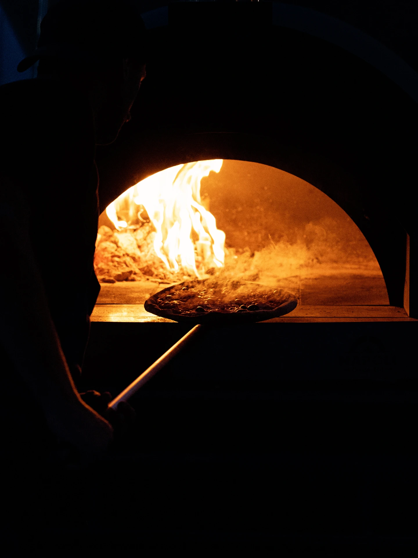 Chef sliding a pizza into the flames of the wood-fired oven